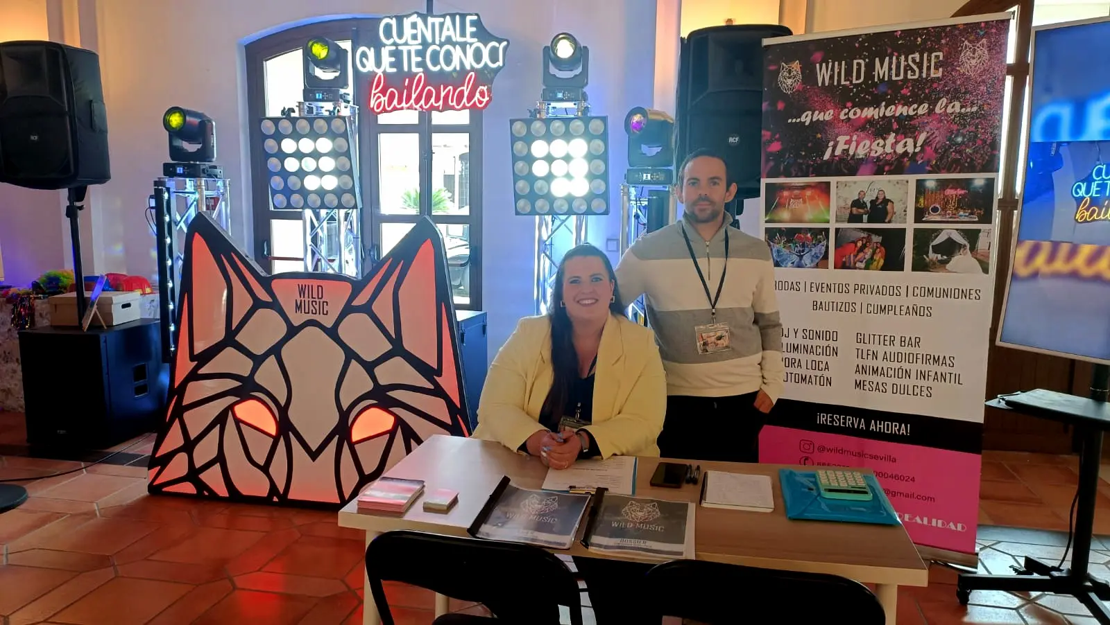 Equipo de Wild Music en mesa informativa con stand de neón y banner de servicios
